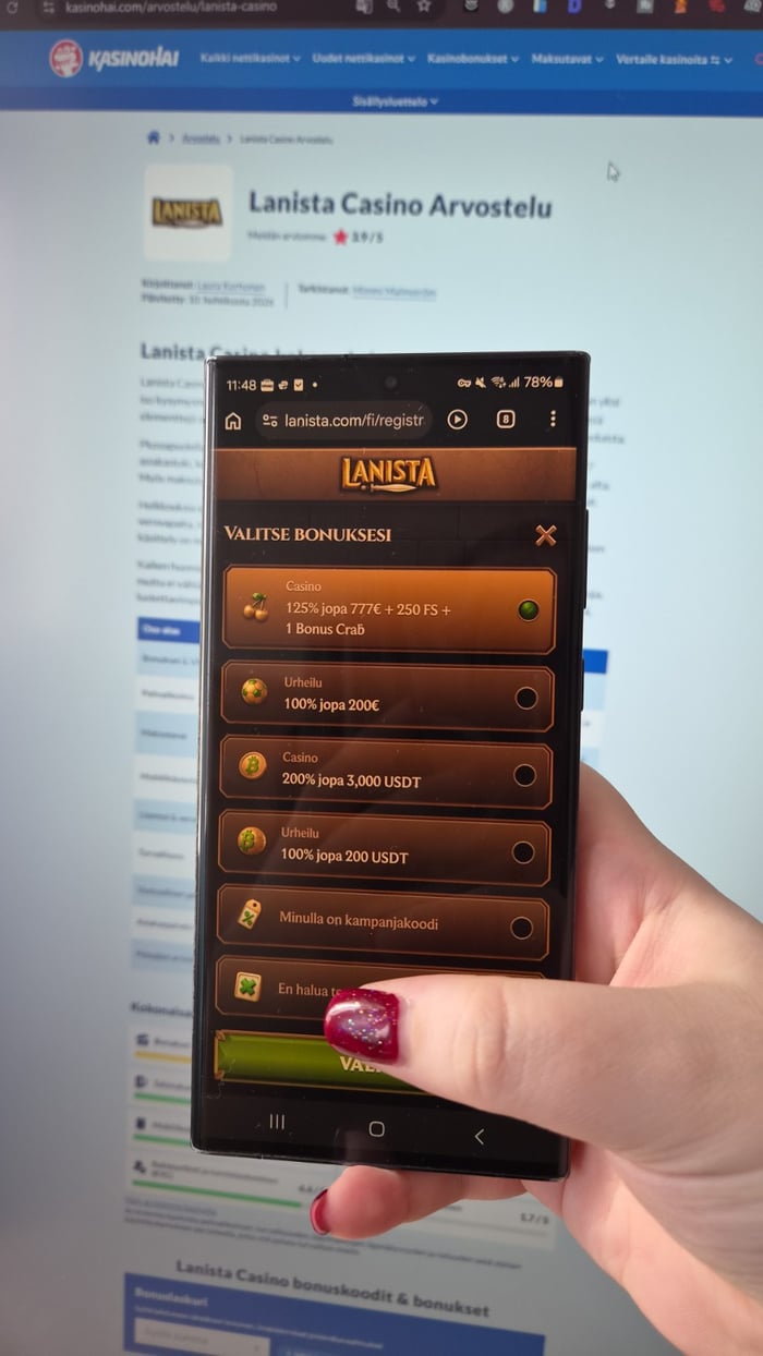 Käsi pitelee kännykkää, jonka näytöllä on auki Lanistan valikko, ja taustalla näkyy tietokoneen ruudulla kasinoarvostelu.