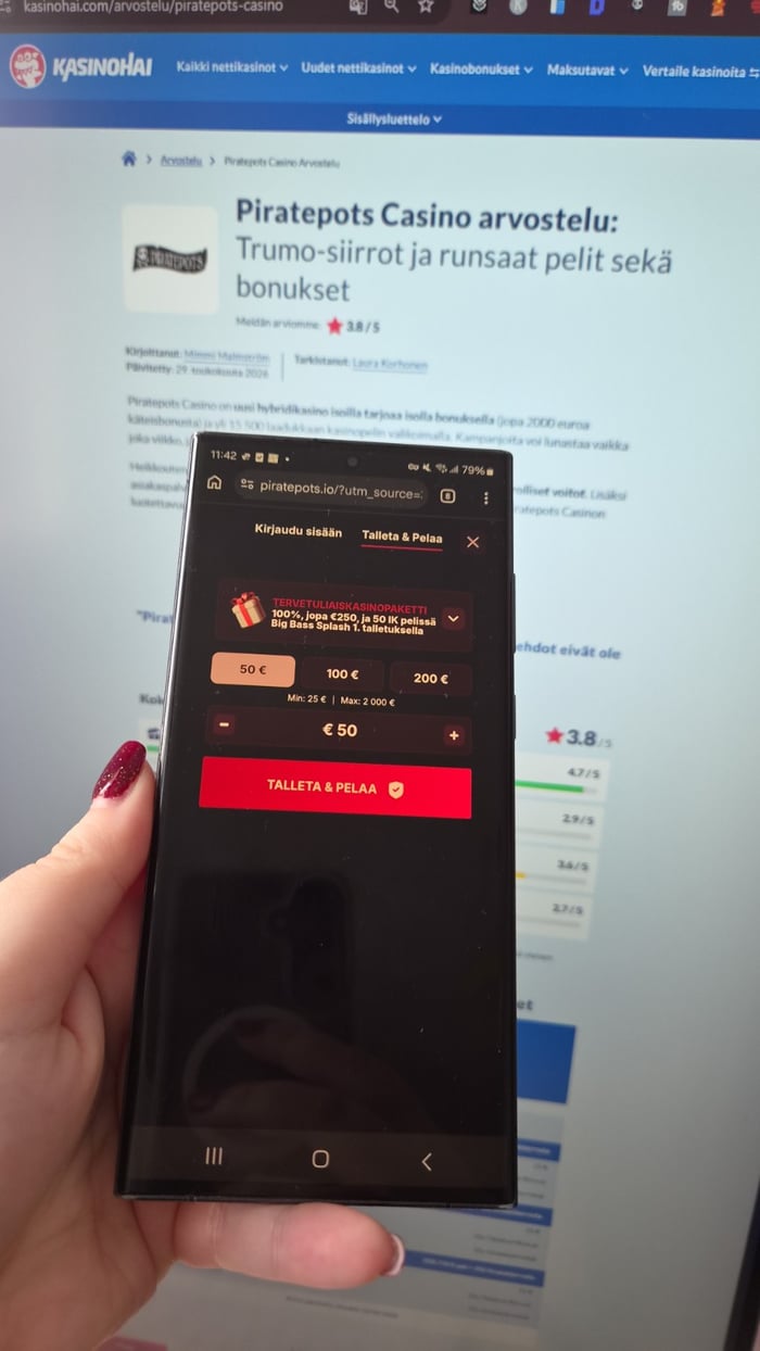 Käsi pitelee puhelinta, jonka näytöllä on auki Piratepots nettikasino, ja taustalla näkyy tietokoneella Kasinohain arvostelu.
